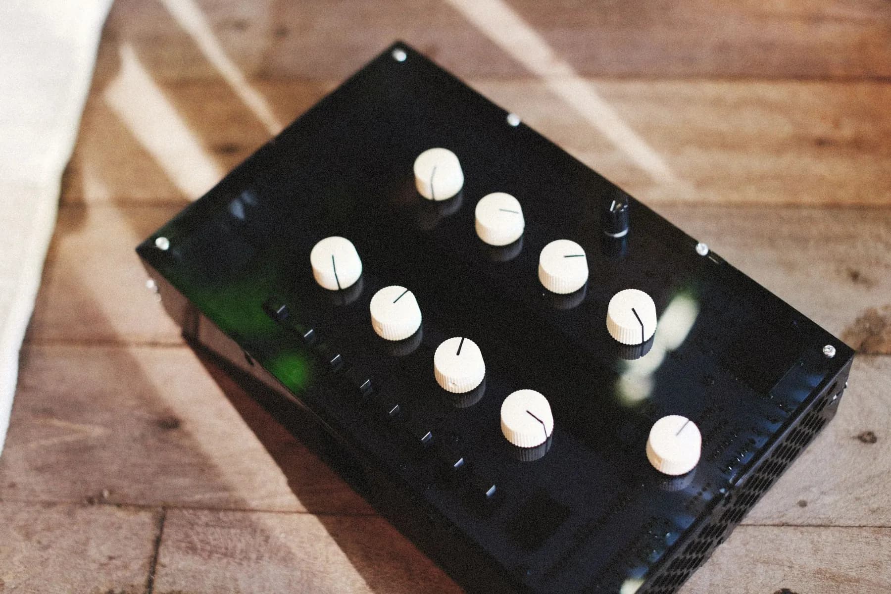 A small controller with cream knobs on a sunlit wooden floor.