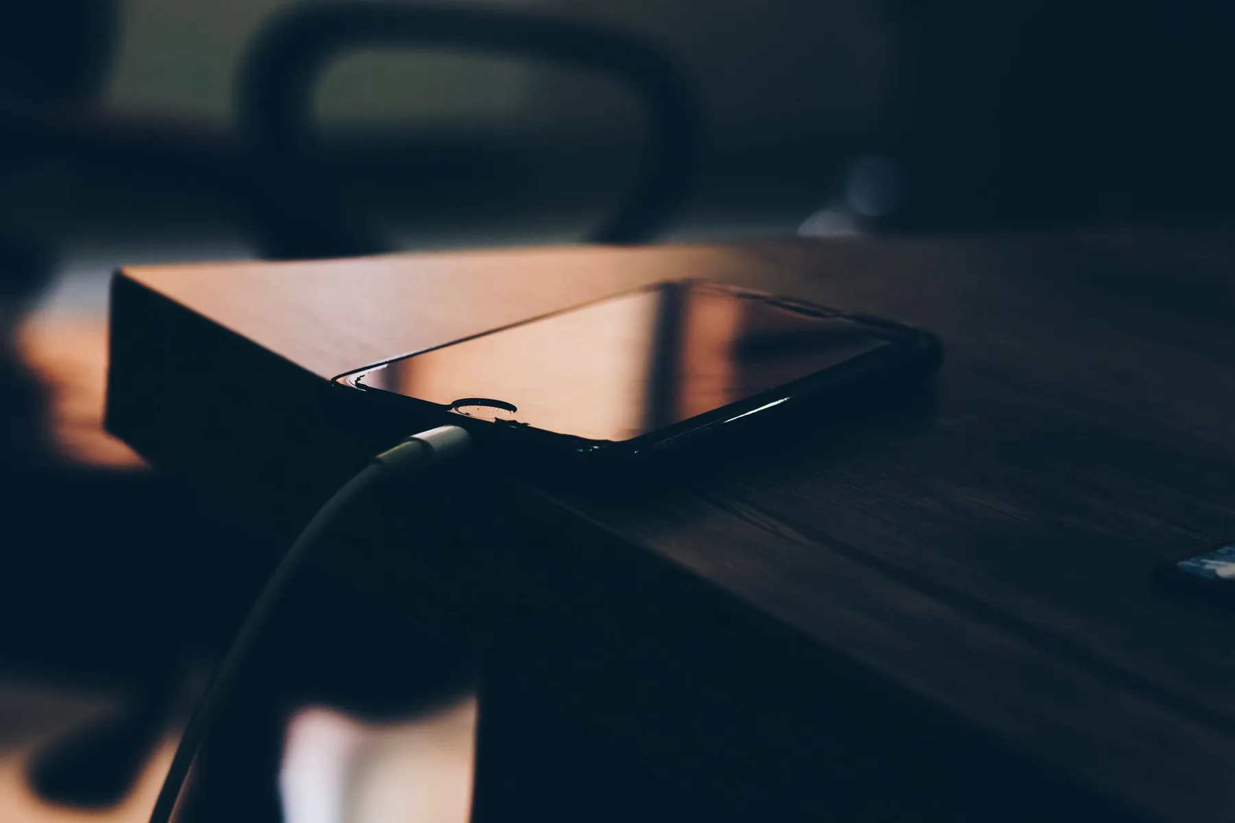 A phone charging on a wooden table in low light.