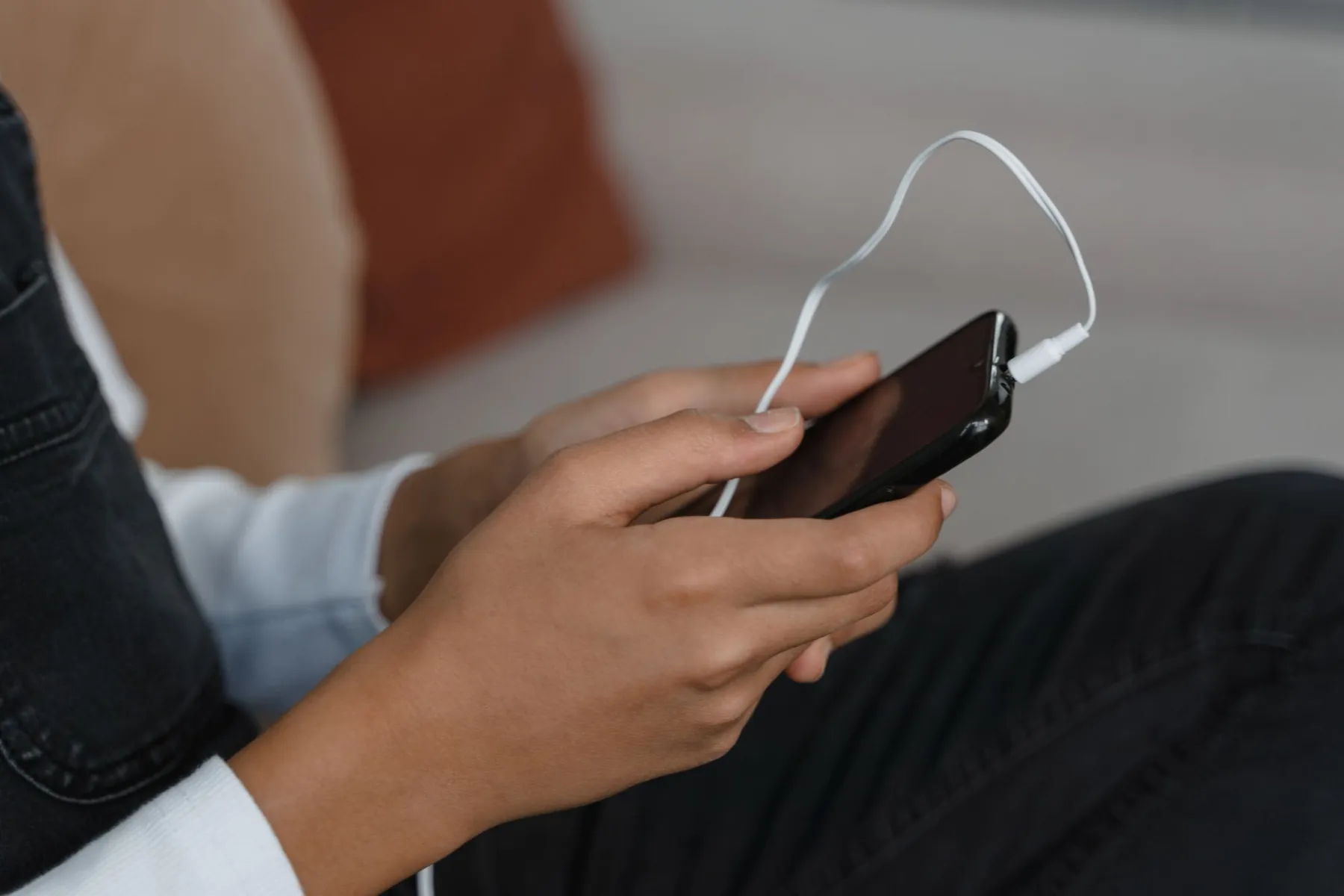 Hands holding a phone with wired earphones plugged in.