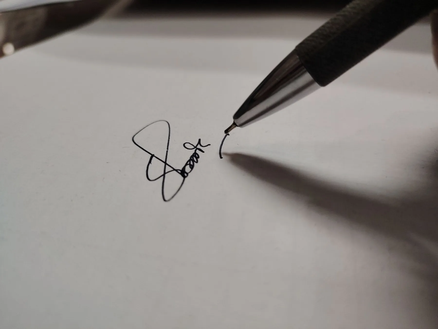 A pen finishing a signature on white paper.