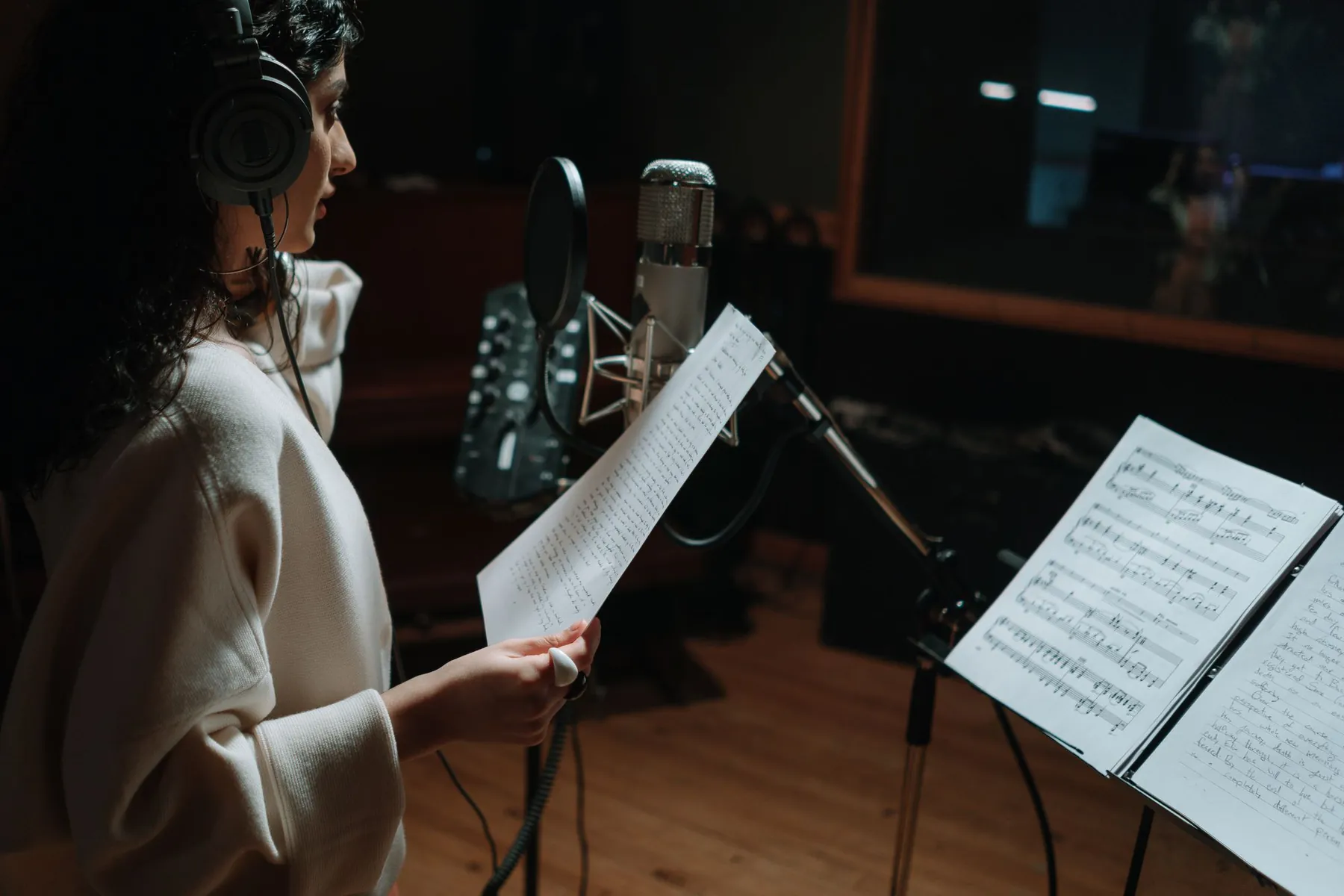 A singer in headphones holding her lyrics at a studio microphone.