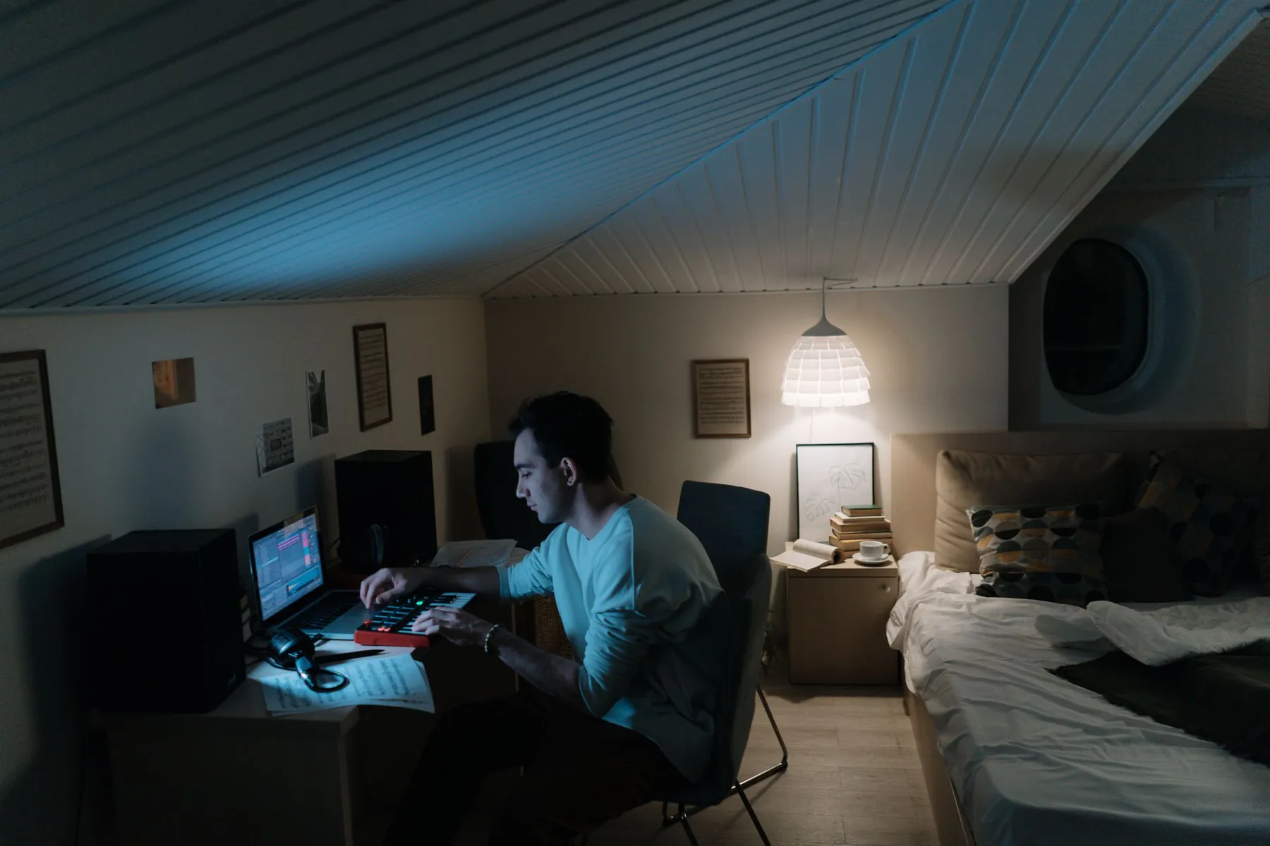 A producer at a laptop and a small keyboard in a bedroom studio at night.